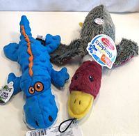 Photo of two plush dog toys: a blue alligator and a grey/red/yellow duck, both new with tags still attached.