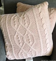 Two pink knit pillows with cable knit pattern on a dark couch.