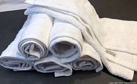 Six white cotton towels rolled and stacked together showing soft texture and edges.