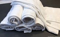 Stack of six rolled white cotton towels showing the softness and thickness of the fabric.