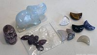 Photo of crystal stones laid out with clear blue hippopotamus, skull, bag of small purple stones and crescent-shaped polished pieces