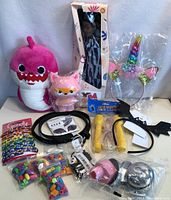 Photo showing pink plush shark, pink fox toy, boxed doll, unicorn headband, black bat headbands, yellow toy dumbbells, stickers, and various costume accessories.
