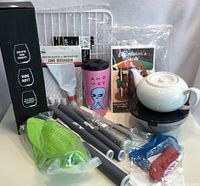 Photo of all kitchenware items including boxed wine glasses, cake decorator set, teapot, silicone lids, strainer, pink travel mug, and cookbook.