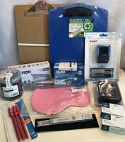 Full view of all office supplies in the lot, showing clipboards, stapler, stamps, pens, paper clips, dry erase markers, eye mask, and utility knife.