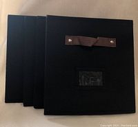 Four black Decomomo cube storage bins stacked side by side on a surface showing front side with handle and label holder.