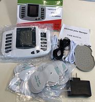 Photo of electronic pulse massager device, electrode pads, cables, power adapter, user manual, and massage pad all new in box and sealed plastic.