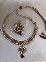 Photo showing ladies necklace and earrings set with clear and red stones on gold-tone metal with fabric cord