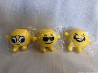 Photo showing three yellow emoji stress balls, each with different facial expressions and small limbs, wrapped in plastic.