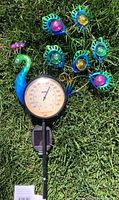 Peacock garden stake with brightly colored solar lights and a built-in thermometer in the grass.