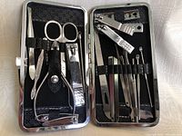 Opened black manicure case showing 19 metal manicure tools attached by elastic bands, including scissors, tweezers, and nail clippers.