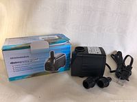 Photo showing the submersible pump next to original box and two hose fittings, with attached power cord.