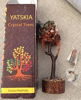 Box labeled 'Yatskia Crystal Trees' with tagline 'Enroot Positivity', showing tree sculpture and two crystal accessories on beige fabric.