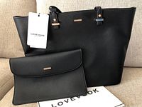 Front view of the new black Lovevook purse with attached tags and matching clutch placed on cloth with brand name.