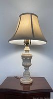 Full view of the lamp on a wooden surface against a wall, showcasing its alabaster base and cream shade