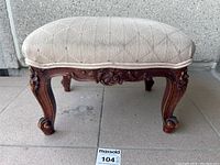 Front view of antique footstool showing upholstered beige seat and carved cabriole legs.