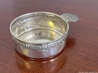 Top angle view showing floral patterned rim and small handle with floral design, reflective surface with some tarnish inside