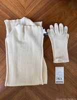 Cream cashmere scarf folded and one glove with tag displayed on wooden surface.