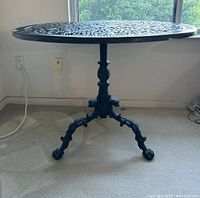 Front photo showing round cast aluminum table with ornate legs and a glass top.