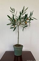 Front view of faux lemon tree plant showing shaped branches with green and gray-green leaves and small yellow lemons, in decorative green ceramic pot
