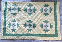 Full view of the handmade yellow, green, and white quilt laid flat showing geometric star patterns and green border