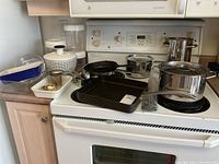 Full kitchen lot displayed on stove and counter, showing various pots, pans, and bakeware items.