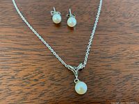 Close-up of pearl stud earrings and pearl pendant on sterling silver chain against wooden background