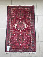 Full view of the vintage Persian carpet showing its rectangular shape, dominant red color, central geometric medallion, and patterned borders.