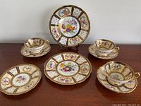 Full set of 3 cups and 3 saucers arranged on wooden surface with one extra plate behind them showing the pattern and design