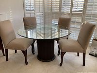 Four dining chairs arranged around a round glass top table in a room with shuttered windows.