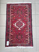 Full view of small rectangular Persian rug on tiled floor showing overall geometric design with a central medallion and layered borders.