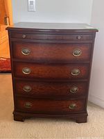 Front view showing bowfront design, four drawers, bracket feet, and brass bail pulls
