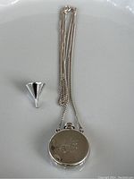 Pendant, chain, dabber and funnel laid out on white surface