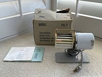 Photo showing Braun HL1 desk fan with its original box and manual on a floor surface near windows.