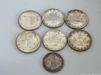 Overview of all six silver dollars and one fifty-cent coin arranged on neutral background.
