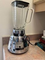 Full blender front view showing glass pitcher, handle, and chrome base with controls.