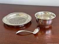Group view of crystal butter dish on silver base alongside sterling sugar bowl and Birks spoon on wooden surface