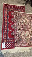 Photo showing both area rugs together, one red with floral motifs and one cream with medallion pattern.
