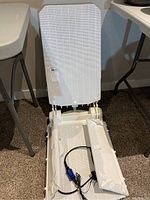 Full view of white bath assist chair in upright position with remote control lying on seat