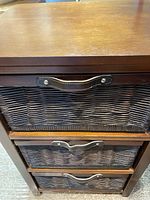 Front view showing the three woven cane basket drawers with leather handles within the wooden cabinet frame.