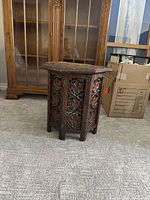 Full view of the dark stained hexagonal wooden end table standing on carpet, showing the carved leaf and grapevine panels.