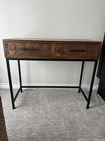 Front view of the entry table showing wood top, two carved drawer fronts with metal handles, and metal frame.
