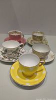 Photo of five fine china teacups and saucers displayed in a group with various floral and decorative patterns.