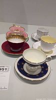 View of all five fine china teacups with matching saucers in varying colors and patterns on display