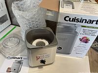 Full view of the ice cream maker body with clear lid and original box in the background showcasing product branding and details.