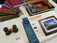 Photo showing the Sylvania digital photo frame box, vintage opera glasses, vintage books, and bar set items on a table