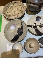 Seven items displayed on tabletop: crock pot, plates, bowls, mortar with pestle, vase