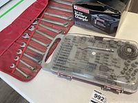 Photo of open-end wrenches in red roll-up pouch along with the battery charger box and drill bit set