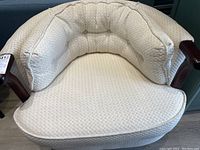 Front view of cream/off-white textured fabric tub chair showing padded back, tufting, and wooden armrests.