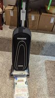 Front view of Oreck upright vacuum cleaner showing black fabric bag with white lines and Oreck logo, carrying handle, and cleaner base.