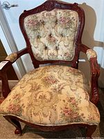 Front view of vintage wooden frame chair with floral patterned button tufted upholstery on backrest and seat cushion.